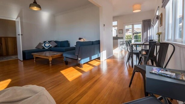 A modern living room with a sofa, coffee table, and dining area with chairs. - Greenview Retreat - Central, Heating, Sleeps 6 (Rotorua)