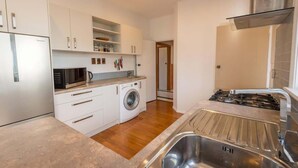 A modern kitchen with white cabinets, a built-in washing machine, a microwave, and a stainless steel sink. - Greenview Retreat - Central, Heating, Sleeps 6 (Rotorua)