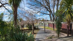 A pathway leading to a building with a covered area, surrounded by various trees and plants. - Greenview Retreat - Central, Heating, Sleeps 6 (Rotorua)