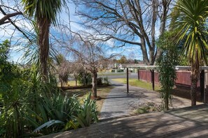 A pathway leading to a building with a covered area, surrounded by various trees and plants. - Greenview Retreat - Central, Heating, Sleeps 6 (Rotorua)