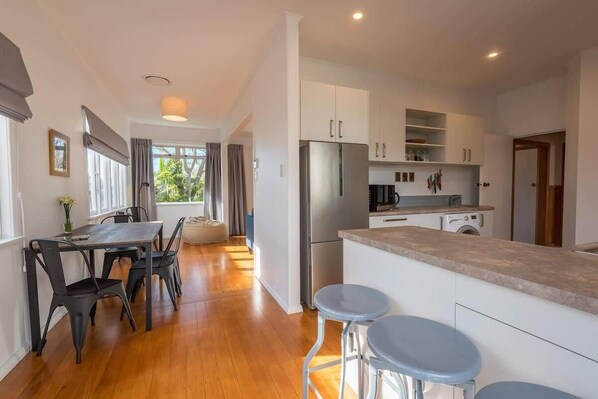 A modern kitchen with a stainless steel refrigerator, white cabinets, and a wooden dining table with chairs.