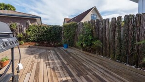 A wooden deck with a barbecue grill, surrounded by a wooden fence and dense foliage. - Greenview Retreat - Central, Heating, Sleeps 6 (Rotorua)