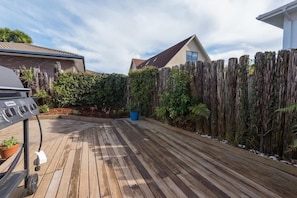 A wooden deck with a barbecue grill, surrounded by a wooden fence and dense foliage.