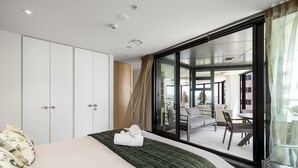 Een moderne hotelkamer met een groot bed, een groene sprei, een wit kussen, een kledingkast en een schuifdeur naar een balkon met uitzicht op de stad.