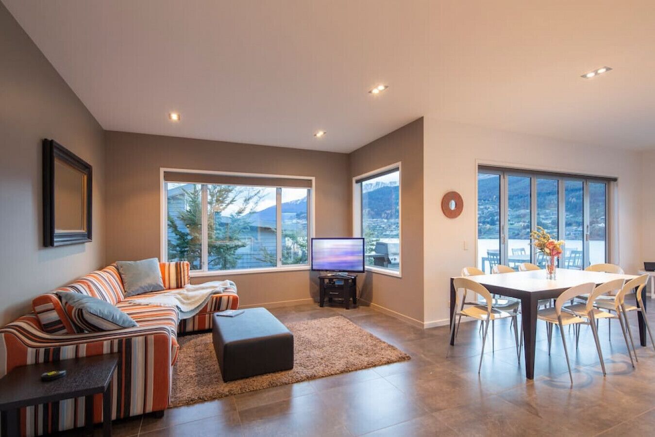 A modern living room with a sofa, TV, and dining area with chairs and a table.