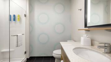 Une salle de bain avec une douche à parois de verre, un lavabo blanc avec un miroir et des toilettes avec un mur décoré de motifs.