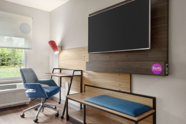 A modern room with a large TV, a blue chair, a wooden desk, and a bench.