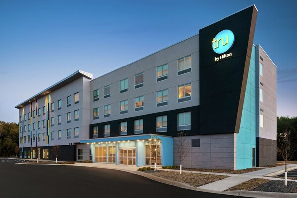 A modern hotel building with a prominent 'tru by Hilton' sign, multiple entry points, and a well-lit facade.