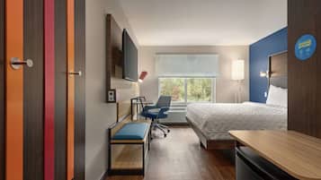 Hotelkamer met een bed, bureau, stoel, televisie en een raam met uitzicht op bomen.