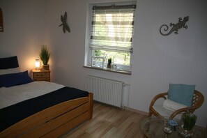 A bedroom with a bed, a chair, a window with a view, a radiator, and wall decorations.