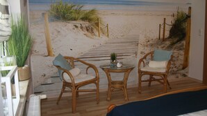 A room with a beach view mural, wicker furniture, and a small table with a plant. - Vacation home at the edge of the forest Biendorf near Kühlungsborn - 2-room vacation home (70m², max. (Biendorf)