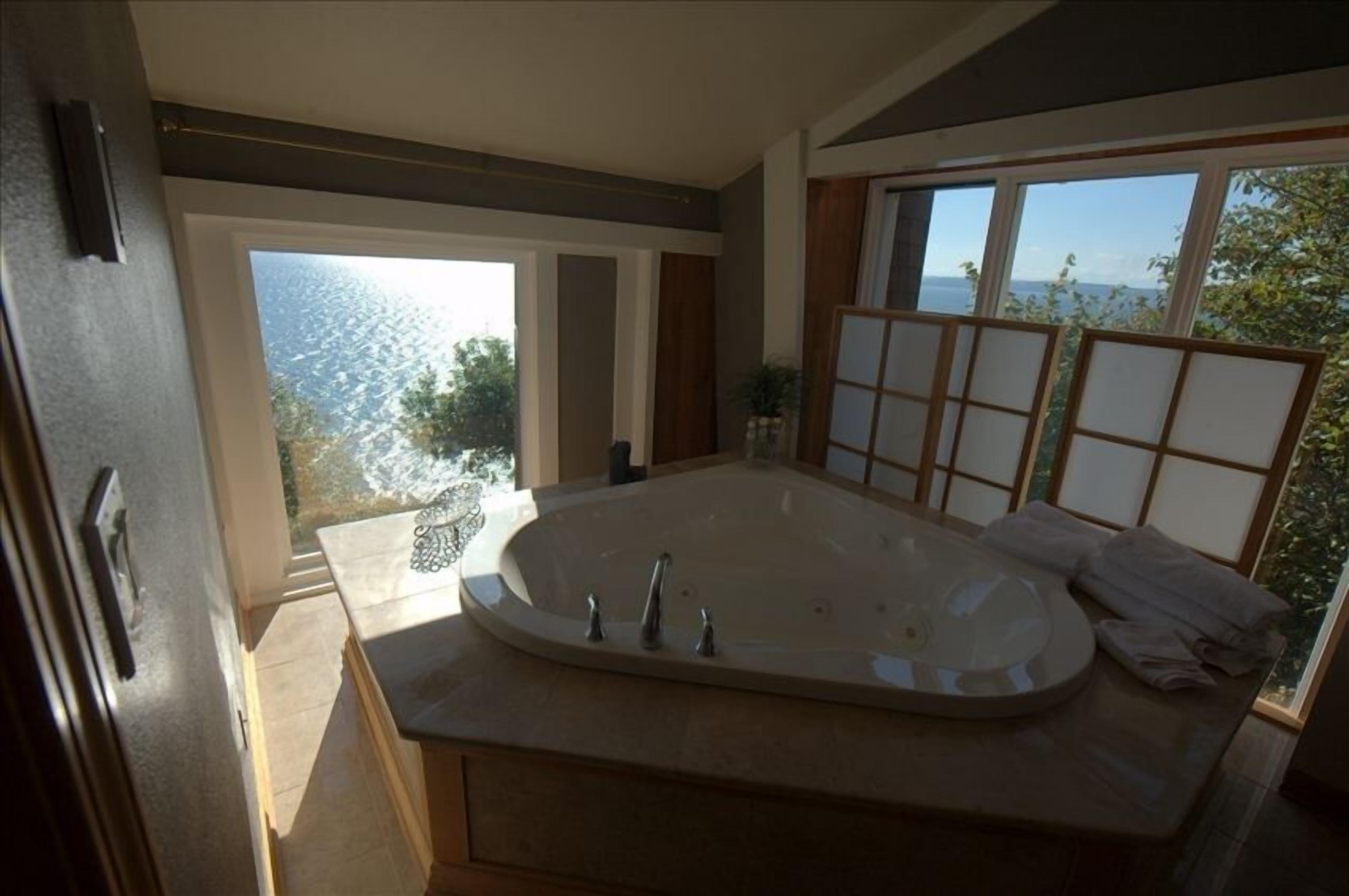 A modern bathroom with a large bathtub, a view of the sea, and a sliding glass door leading to an outdoor area.