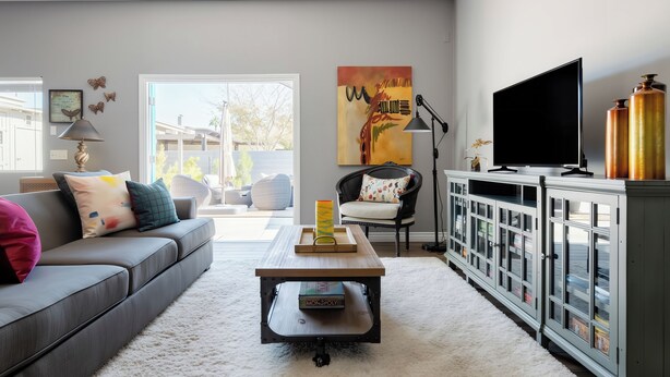 A modern living room with a grey sofa, a coffee table, a TV, and a cabinet with glass doors. - Stay Close to Culture & Sports Venues in a Spacious & Stylish Butterfly Studio (Phoenix)