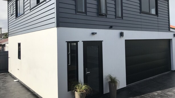 A modern two-story house with a garage, white exterior walls, and dark siding.