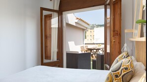 A bedroom with a bed, a window, and a view of the outside balcony area.