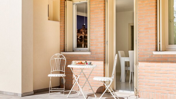 An outdoor seating area with a table and two chairs, a window with a view of a bridge, and a brick wall. - The Romeo country house apartment accommodates up to 5 people (4 + 1) (Cimadolmo)