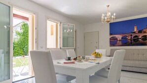 A dining area with a white table and chairs, a chandelier, and a painting of a bridge. - The Romeo country house apartment accommodates up to 5 people (4 + 1) (Cimadolmo)