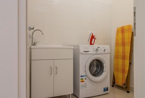 A compact laundry area with a washing machine, a sink, and a drying rack.
