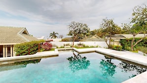 Un área de piscina tranquila con superficie de agua cristalina, rodeada de exuberante vegetación y edificios de estilo tradicional.