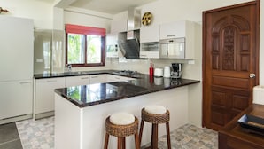 Una cocina moderna con armarios blancos, encimera negra y dos taburetes de mimbre.