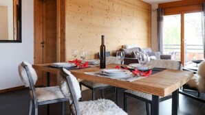 A dining area with a wooden table set for four, chairs with fur throw cushions, and a sofa in the background. - Ferme de Sandra F2 by Interhome (Nendaz)