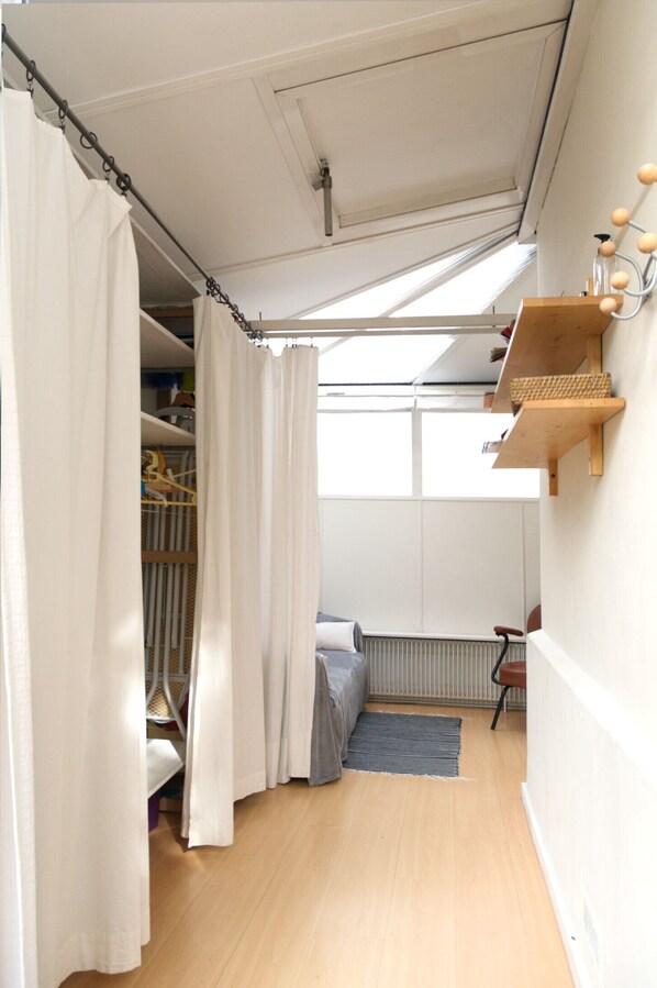 Un dormitorio con tragaluz, suelo de madera, una cama, un radiador y una estantería con objetos.
