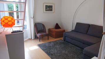 Un salon moderne avec un canapé, un fauteuil et une petite table. On y trouve un escalier avec une rampe, une fenêtre avec des rideaux et un luminaire suspendu.