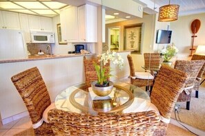 Una cucina moderna con mobili bianchi, un forno a microonde e un'area pranzo con sedie in vimini e un tavolo in vetro.
