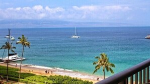 A beach view with palm trees, a sailboat, and yachts in the water. - Tower 1 South facing. Beautiful Ocean, Lanai , koi pond and courtyard views (Lahaina)