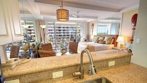 A modern hotel room with a large window, a built-in kitchen counter, and a cozy seating area with a sofa and chairs. - Tower 1 South facing. Beautiful Ocean, Lanai , koi pond and courtyard views (Lahaina)
