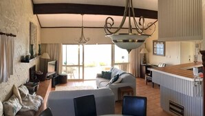 A spacious living room with a glass dining table, a sofa, and a kitchen area with a bar counter.
