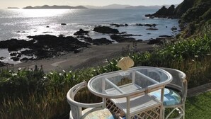A glass-top table with wicker chairs overlooking a rocky coastline with a view of distant islands.