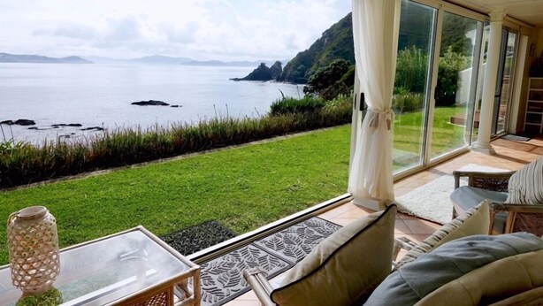 A room with a glass door leading to a grassy area with a view of the sea and hills.