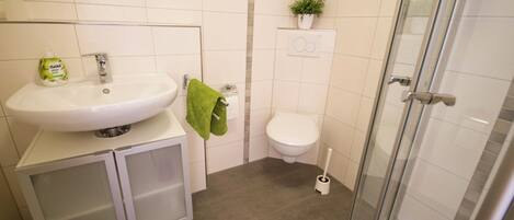 A bathroom with a sink, toilet, shower, and a small potted plant on the wall.