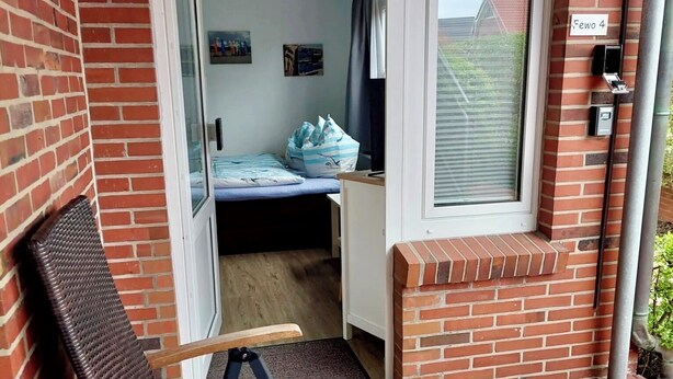 A room with a bed, a window, a door, and a table with a glass object.