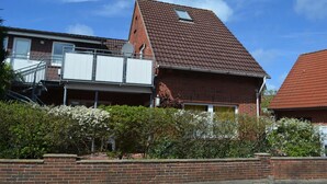 A two-story house with a red-tiled roof, a small balcony, and a brick exterior.
