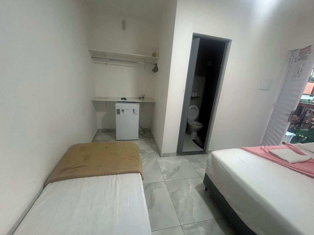 A compact room with two beds, a small kitchenette, and a toilet.