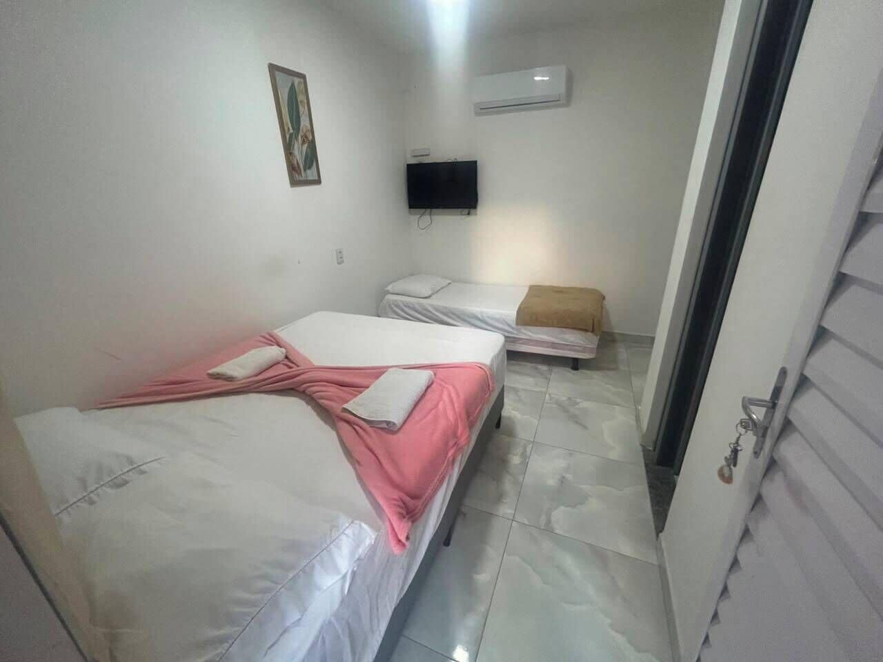 Una habitación pequeña y limpia con dos camas, un televisor de pantalla plana y aire acondicionado.