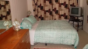 Un dormitorio con cama, cómoda, televisor sobre un mueble bajo y cortinas estampadas.