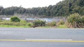 Una carretera con una colina boscosa al fondo y una masa de agua.