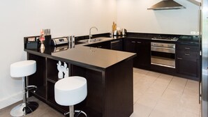A modern kitchen with a central island, stainless steel appliances, and a black countertop. - 3 LEVEL LAKESIDE LUXURY WITH MAGNIFICENT LAKE & MOUNTAIN VIEWS POTENTIAL CARHIRE (Frankton)