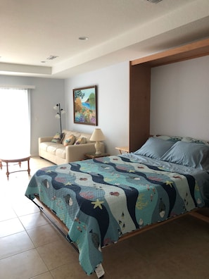 A bedroom with a bed, a sofa, a painting, and a lamp.