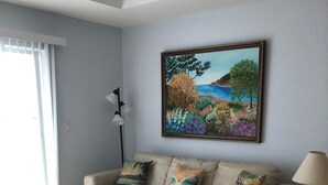 Ein Wohnzimmer mit einem beigefarbenen Sofa, einem Glastisch und einem Landschaftsbild an der Wand.
