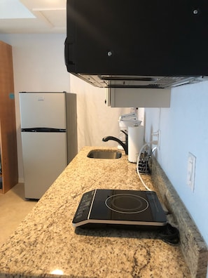 A kitchen with a granite countertop, a built-in oven, a stainless steel refrigerator, and a wall-mounted microwave.
