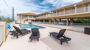 Ein Hotel mit Poolbereich, Liegestühlen und einem zweistöckigen Gebäude mit Balkonen.