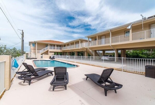 A hotel with a pool area featuring lounge chairs and a two-story building with balconies.