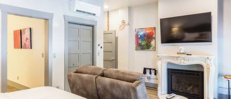 Una habitación de hotel moderna con una cama grande, un sofá, una chimenea y un televisor montado en la pared.