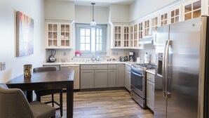 Una cocina moderna con un refrigerador de acero inoxidable grande, horno empotrado y una zona de comedor con mesa y sillas de madera.