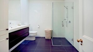 Un bagno moderno con doccia in vetro, un water bianco e un pavimento piastrellato scuro.