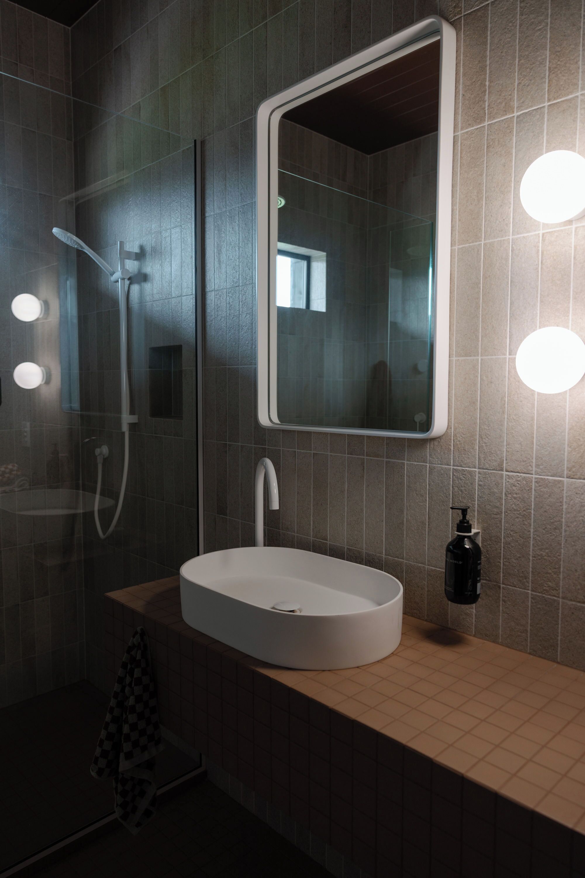 Un baño moderno con ducha de vidrio, lavamanos redondo blanco y espejo con iluminación.